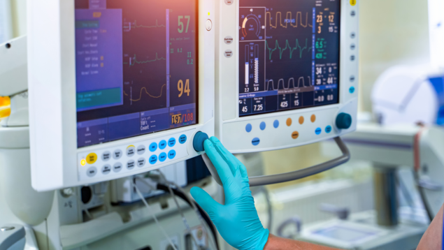 Dame prüft an einem Monitor neben dem Patientenbett die Werte und bedient das Touchpad. 