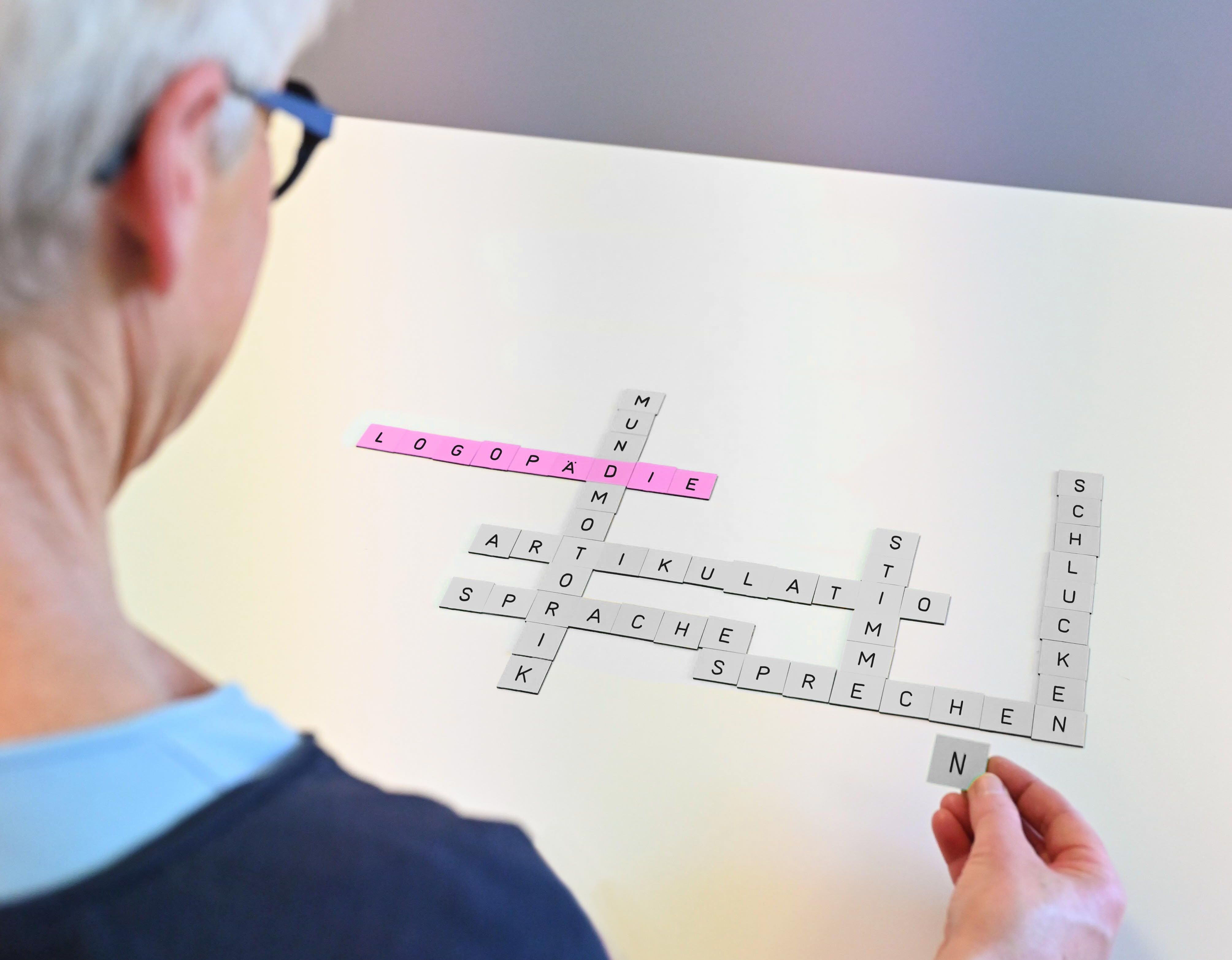 Patientin legt Scrabble-Buchstaben zum Thema Logopädie auf einen Tisch